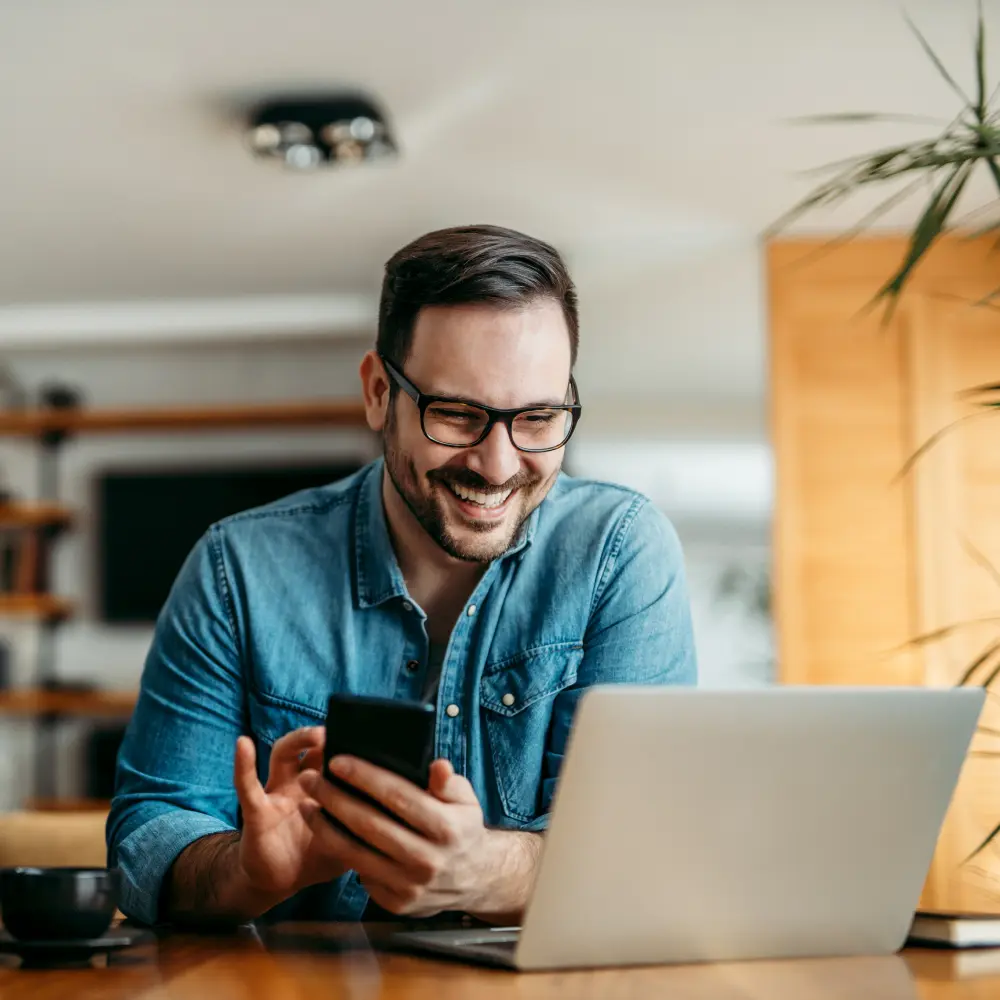 Empreendedor sorrindo enquanto usa o celular e o notebook