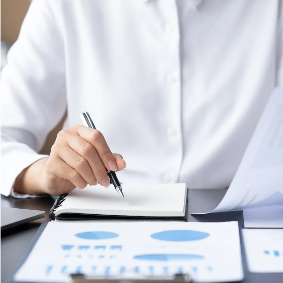 Mãos anotando em um caderno sobre relatórios com gráficos