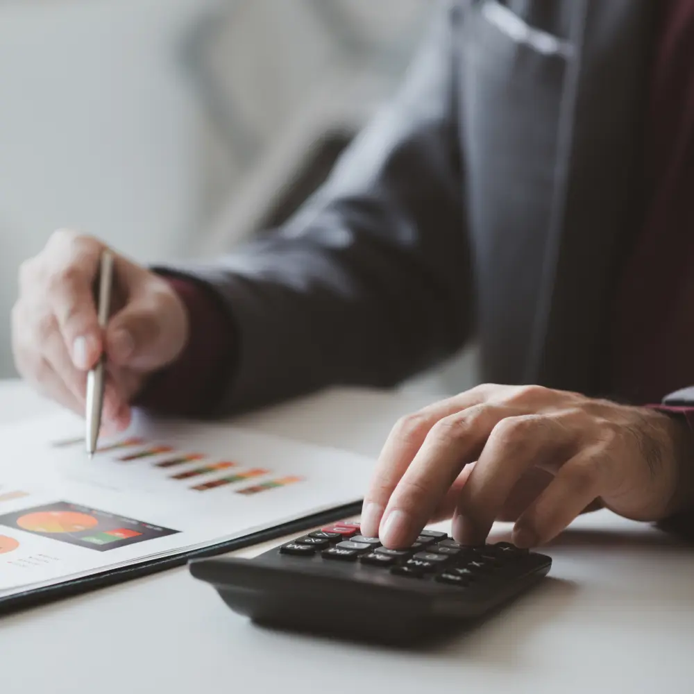 Mãos usando calculadora e caneta sobre relatórios financeiros