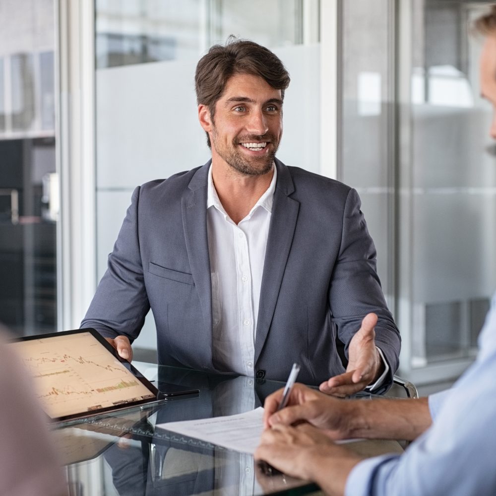 Consultor sorridente em reunião, com um tablet e documentos sobre a mesa