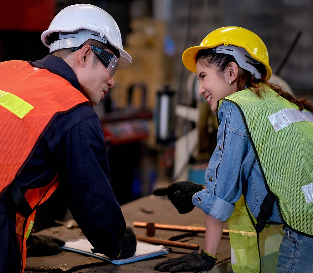 Dois profissionais de capacete e colete conversando em uma oficina industrial